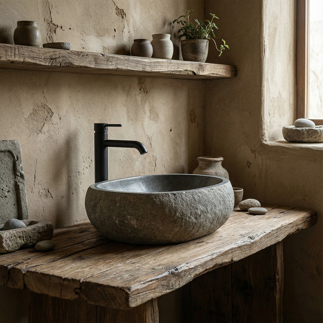 Countertop basin made of river stone in a quiet natural bathroom on an old wooden console, combined with black fittings