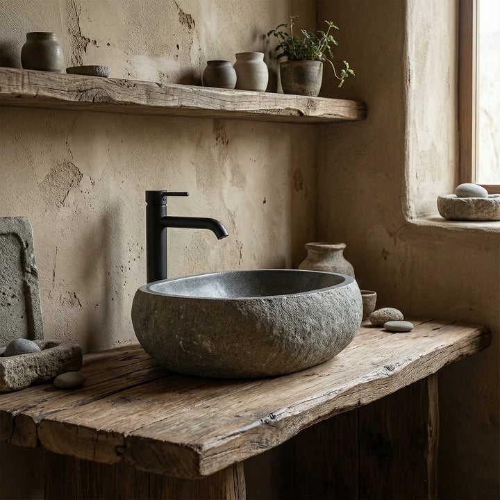 Countertop basin made of river stone in a quiet natural bathroom on an old wooden console, combined with black fittings
