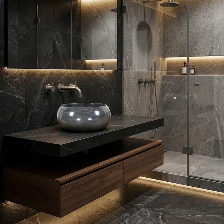 Round countertop washbasin made of natural stone on a dark vanity unit in the modern spa bathroom, combined with wall fittings, glass shower and indirect lighting