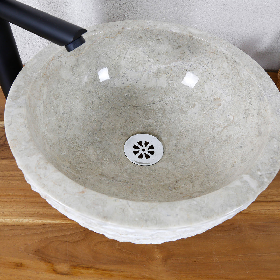 Top view of round countertop washbasin made of natural stone with polished inner surface, rough edge and central drain
