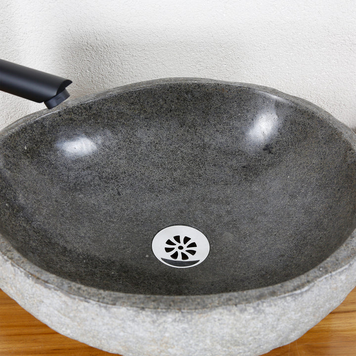 Detailed view of an oval stone sink made of river stone with a finely polished inner surface and a central drain valve