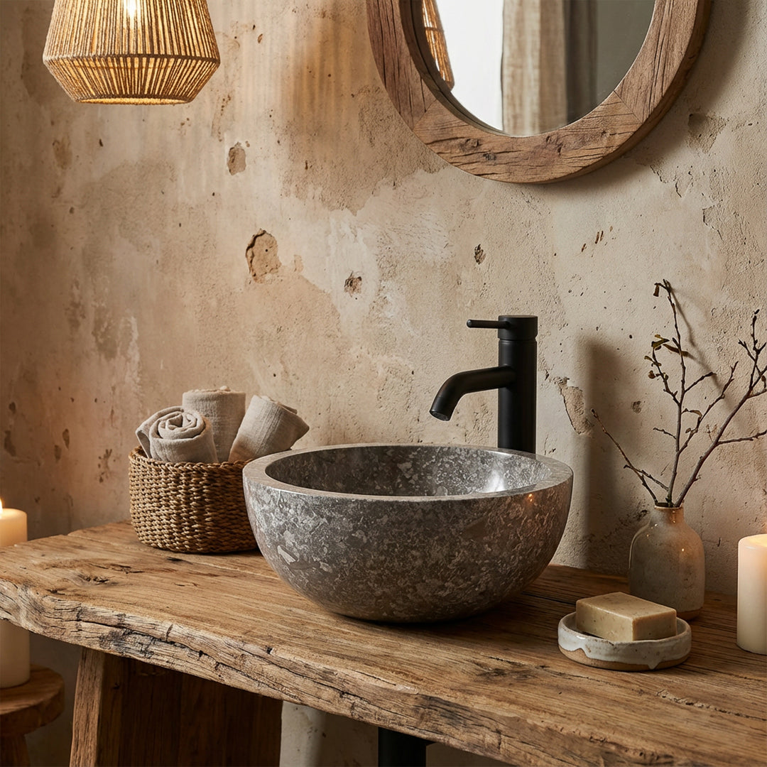 Round countertop washbasin made of stone on a rustic wooden top with black fittings in a natural bathroom ambience