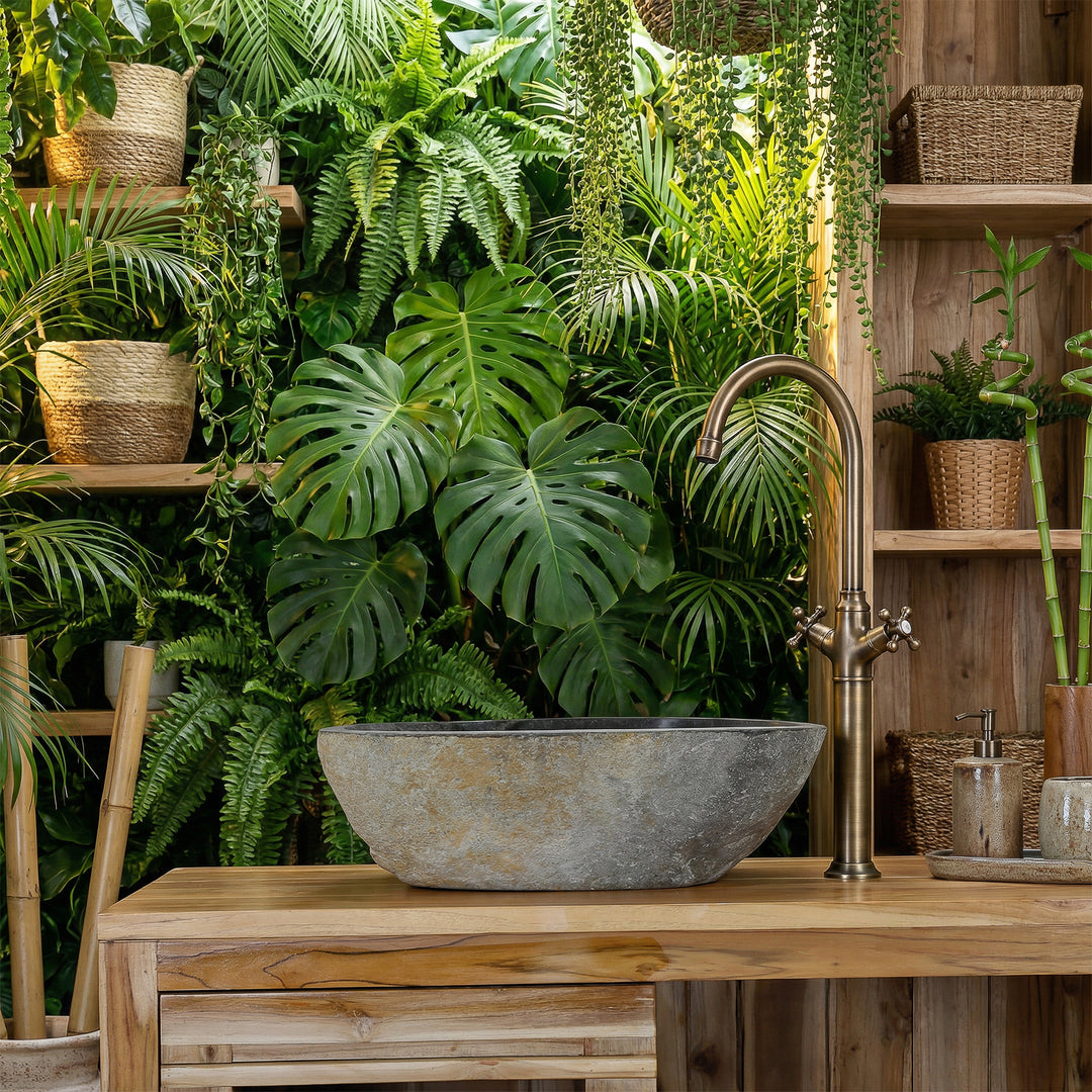 Countertop basin made of river stone in green spa bathroom on wooden vanity unit, combined with brass fittings and lush plant ambience