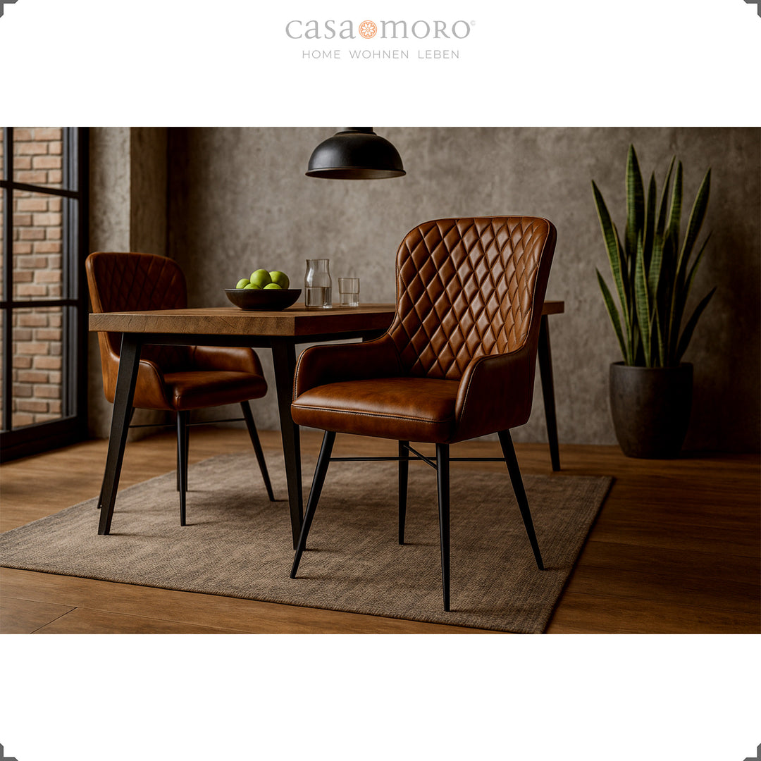 Zwei antikbraune Lederstühle mit Rautensteppung an einem Holztisch im modernen Esszimmer mit Betonwand, Holzboden und grüner Zimmerpflanze.