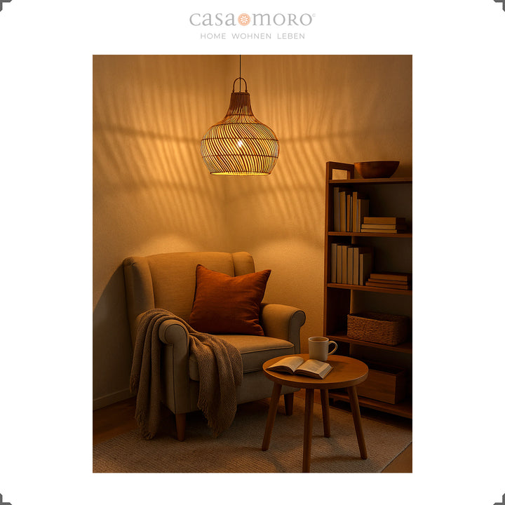 Hängende Rattan-Lampe mit warmem Licht über einem Lesesessel, erzeugt stimmungsvolles Schattenspiel an der Wand