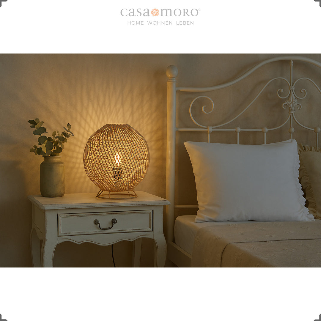 Runde Rattan Nachttischlampe auf weißem Holztisch neben Bett, warmes Licht und sanfte Atmosphäre