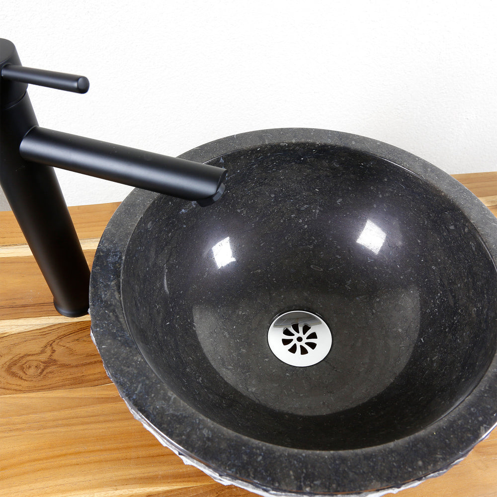 Round countertop basin made of stone in detail with polished inner surface, stainless steel drain and black fitting