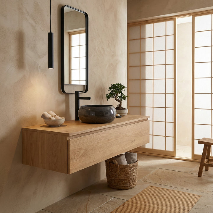 Round stone countertop washbasin on floating wooden vanity unit in Japanese-inspired bathroom, combined with black fittings, wooden frame mirror and soft natural light