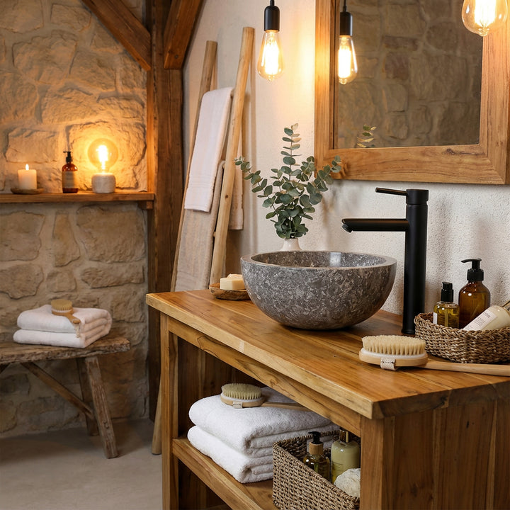Round stone countertop basin on a solid wooden console with black fittings in a warm, rustic bathroom style
