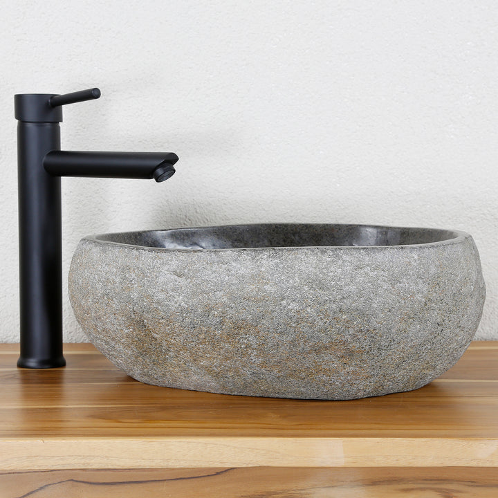 Washbasin Made of gray natural stone in an oval shape, combined with black fittings on a warm wooden top