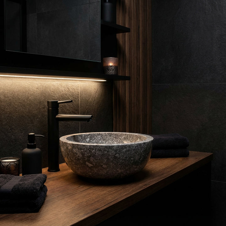 Natural stone Washbasin as a countertop basin on a wooden top, round stone washbasin in a dark bathroom ambience