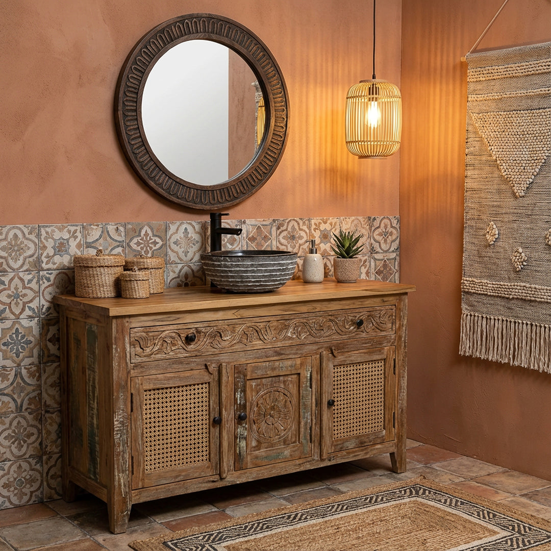 Round stone countertop washbasin on carved wooden vanity unit in warm boho bathroom with tiles, mirror and pendant light
