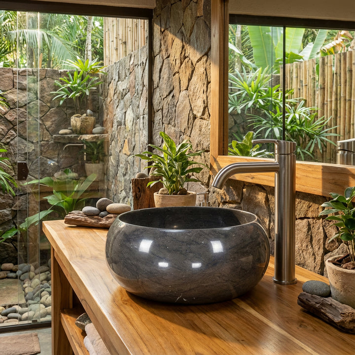 Round Washbasin made of natural stone on a wooden vanity in the open spa bathroom with a stone wall, plants and lots of natural light
