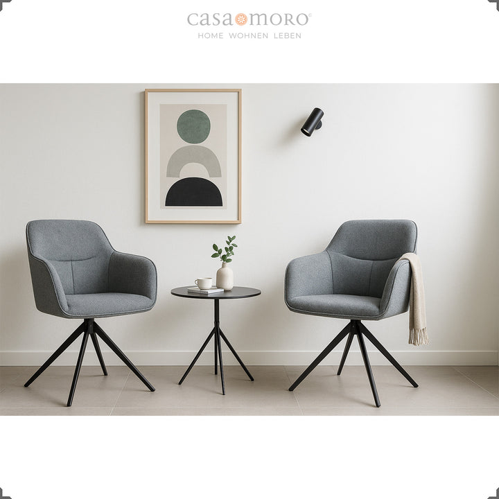 Zwei 360° drehbare Polsterstühle mit Armlehnen in Grau neben einem runden Beistelltisch in modernem Wohnraum mit heller Wanddekoration