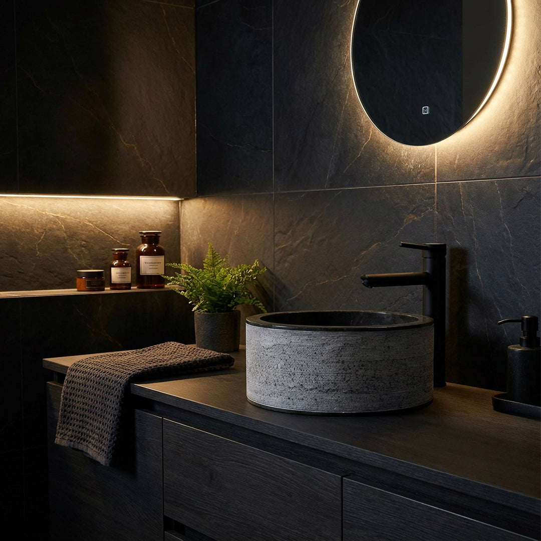 Round stone washbasin with a fine structure on a dark wooden console, atmospherically staged in the modern dark mood bathroom.