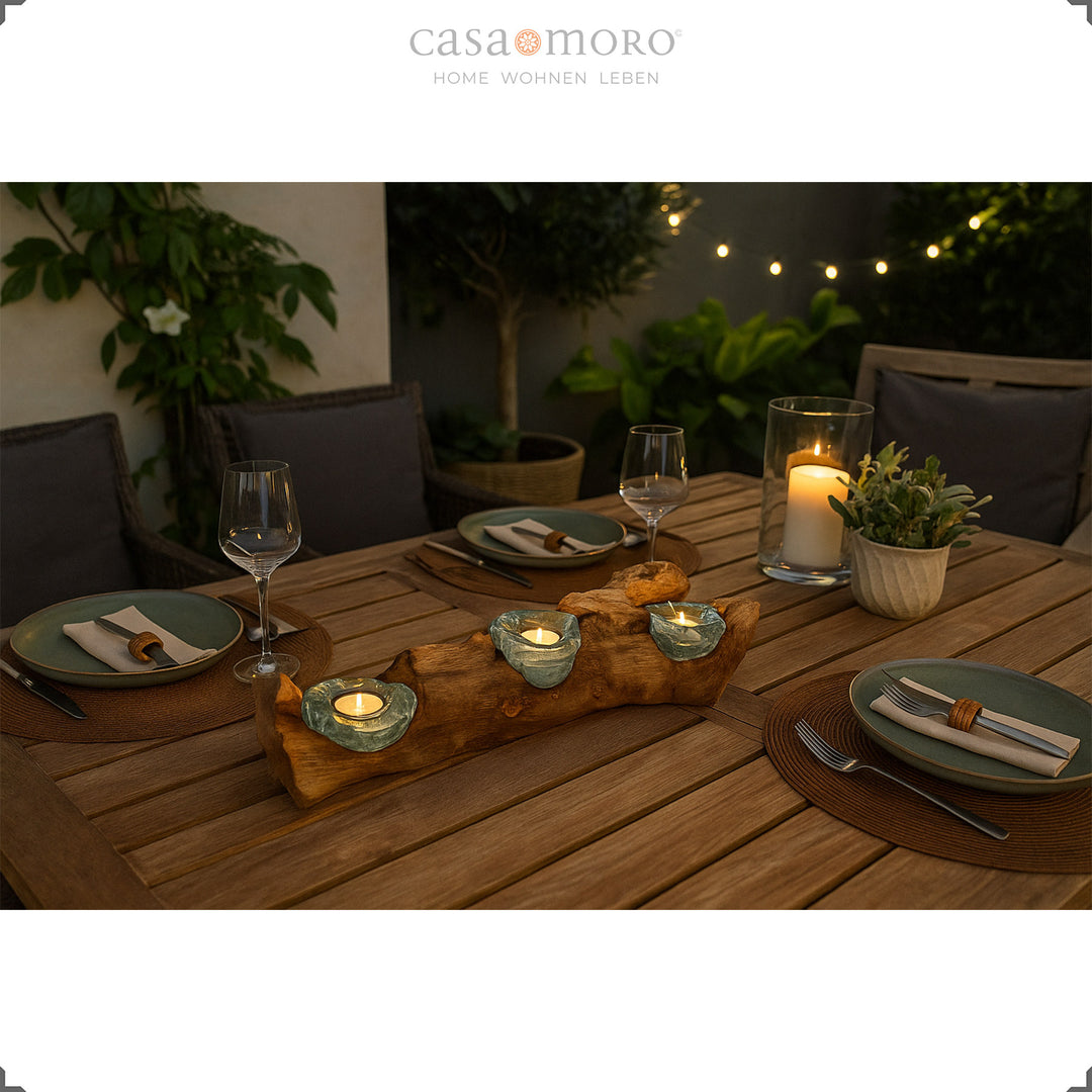 Dreiteiliger Teelichthalter aus Glas und Wurzelholz als stimmungsvolle Tischdeko auf einer Terrasse, eingerahmt von Pflanzen und gedecktem Tisch