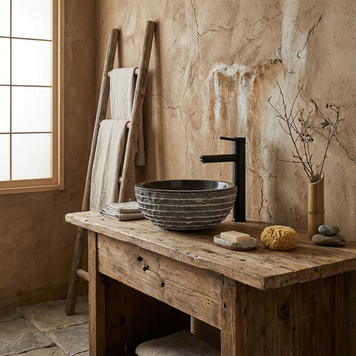 Round natural stone sink on rustic wooden table in tranquil spa bathroom with black faucet and warm natural light