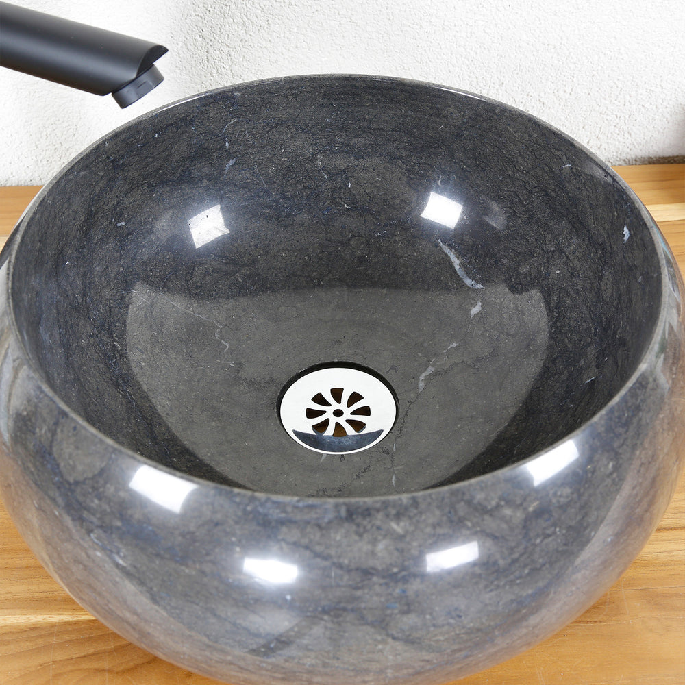 Round Washbasin Made of stone in a detailed view with dark grain, polished inner surface and stainless steel drain, shown on a wooden plate