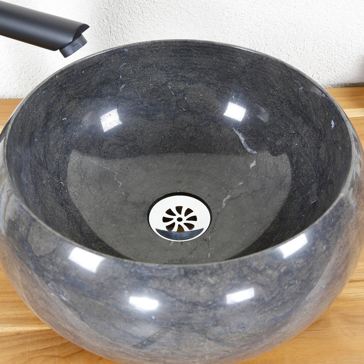 Round Washbasin Made of stone in a detailed view with dark grain, polished inner surface and stainless steel drain, shown on a wooden plate